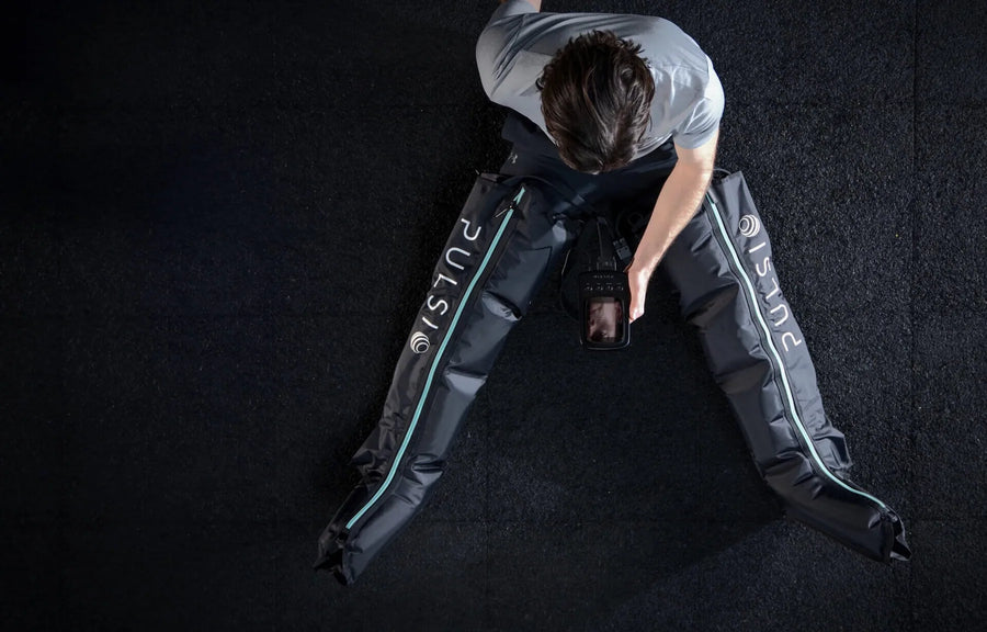 Person using leg compression therapy sleeves while sitting on the floor.